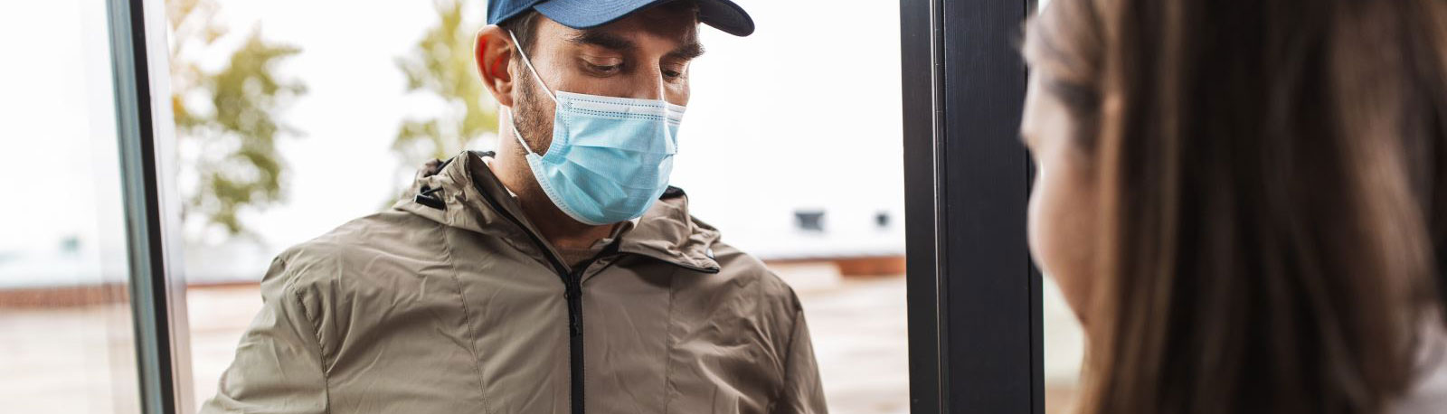 A delivery man wearing a surgical mask talking to a woman in the foreground